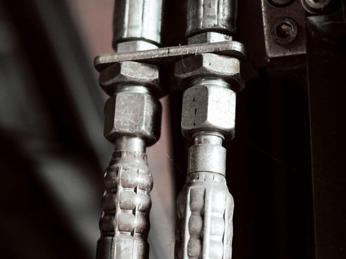 Two metal hydraulic connectors are attached to black rubber hoses. The connectors have a textured grip and are secured tightly, indicating a robust connection. The background is dark, emphasizing the metallic sheen of the connectors and the smooth surface of the hoses.