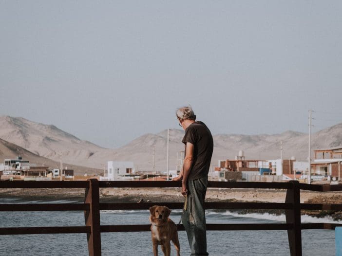 A man and his dog stand by the water.