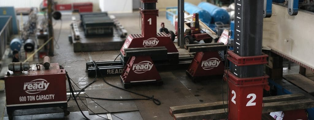 Red heavy machinery equipment labeled "ready" with a 600-ton capacity, including large support stands numbered 1 and 2, situated in an industrial workshop with various tools and equipment in the background.