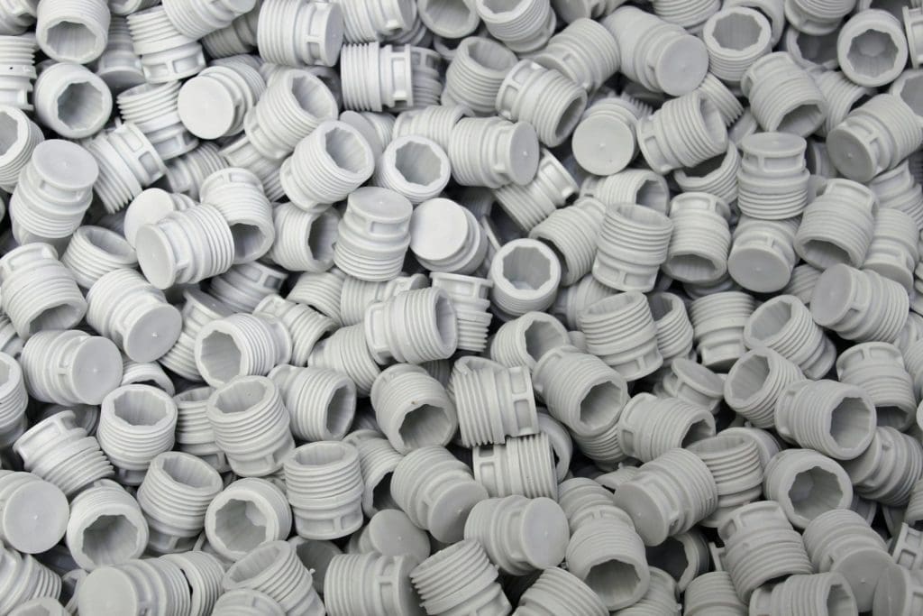 A large pile of small, gray plastic threaded plugs or caps with ridged sides and flat tops, some showing hollow interiors with a star-shaped pattern.