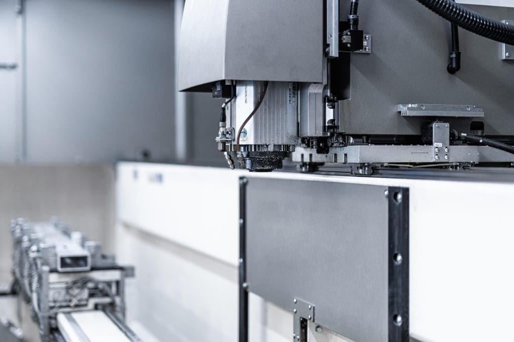 Close-up of a CNC machine spindle head in a manufacturing or industrial setting, showing metal components and wiring with a blurred background.